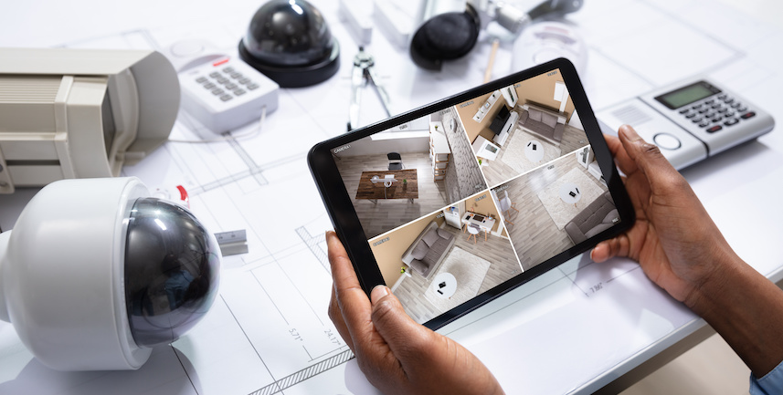An Elevated View Of Person Watching Footage On Digital Tablet With Security Equipment On Blueprint